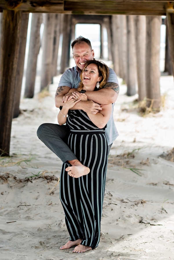 A silly engaged couple having fun under the pier in Long Beach Island, NJ.